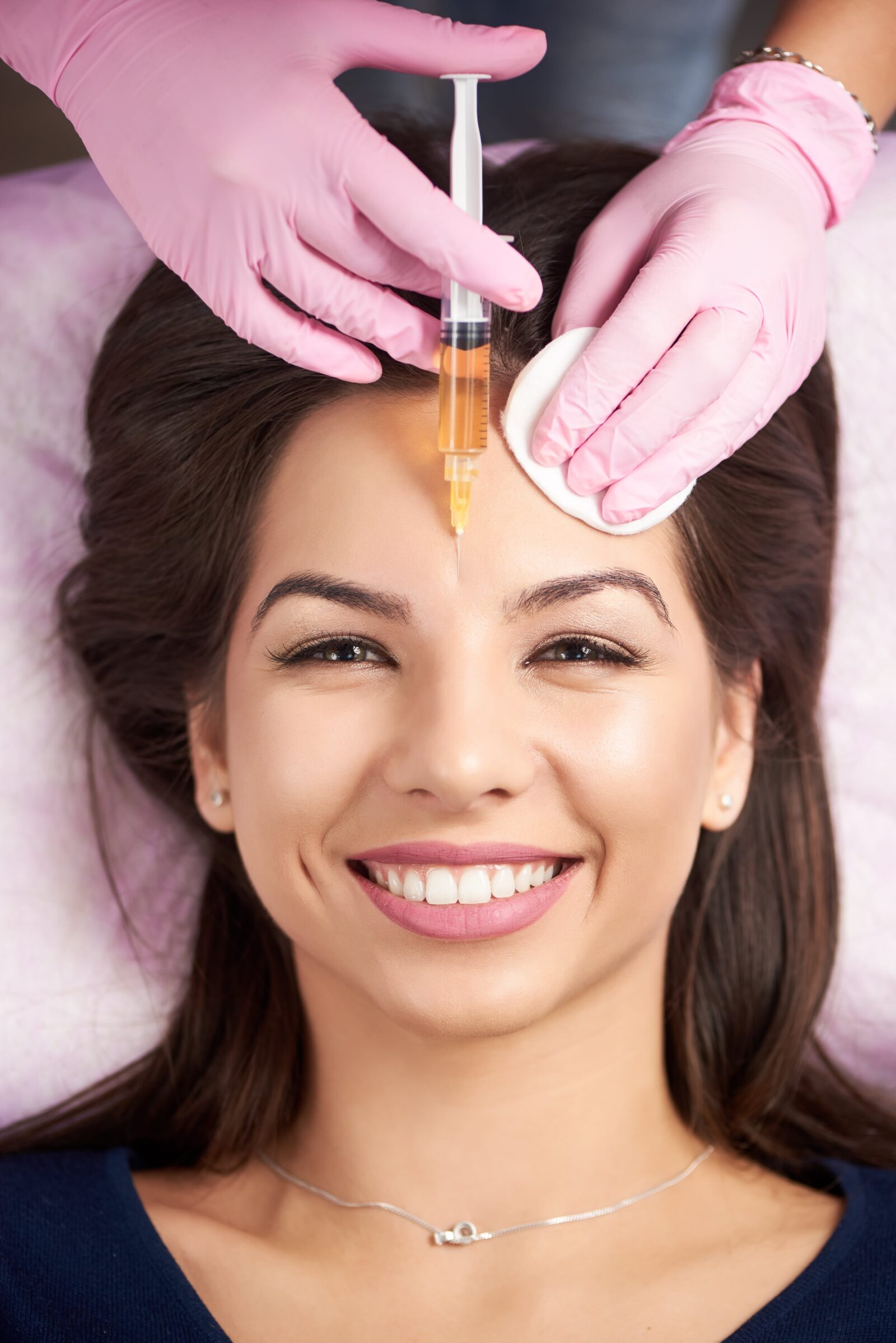 smiling woman having dermal fillers injected into her forehead